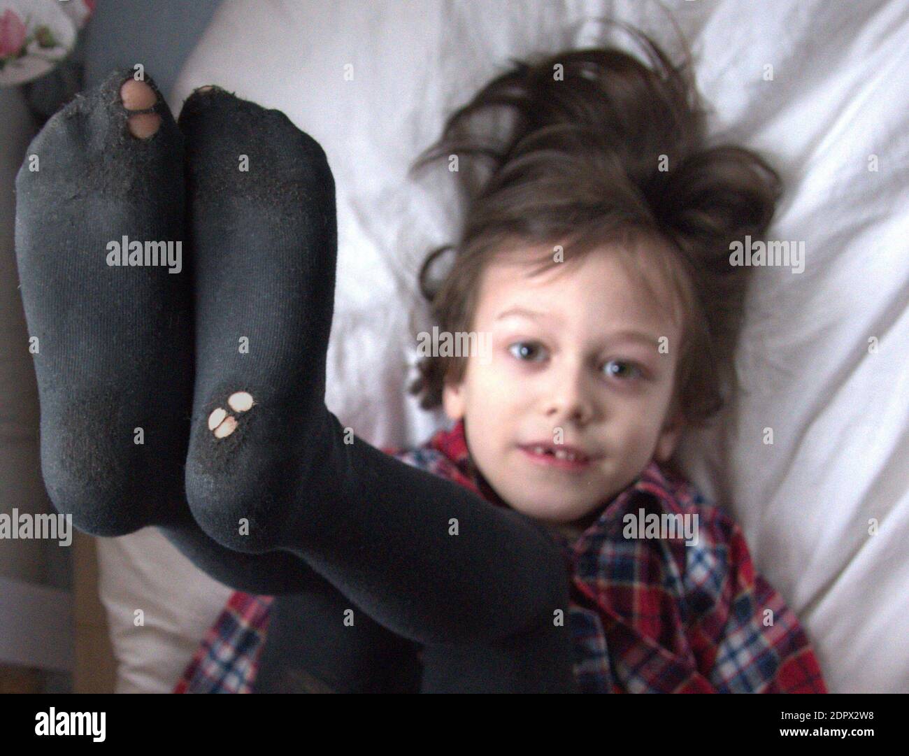 High Angle Portrait Of Boy Wearing Socks While Lying On Bed Stock Photo