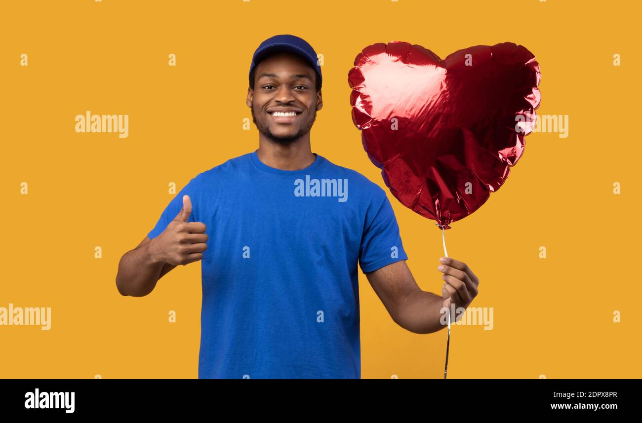 Black delivery man holding balloon and gesturing thumb up Stock Photo