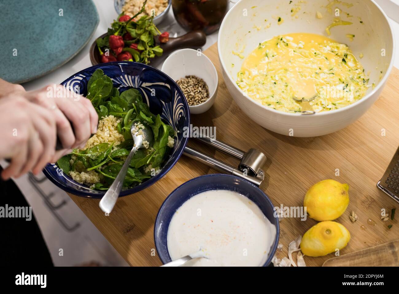 Close up of woman hands garnishing a fresh vegetarian salad with cous cous. Woman cooking in the kitchen at home preparing healthy food. Mediterranean Stock Photo