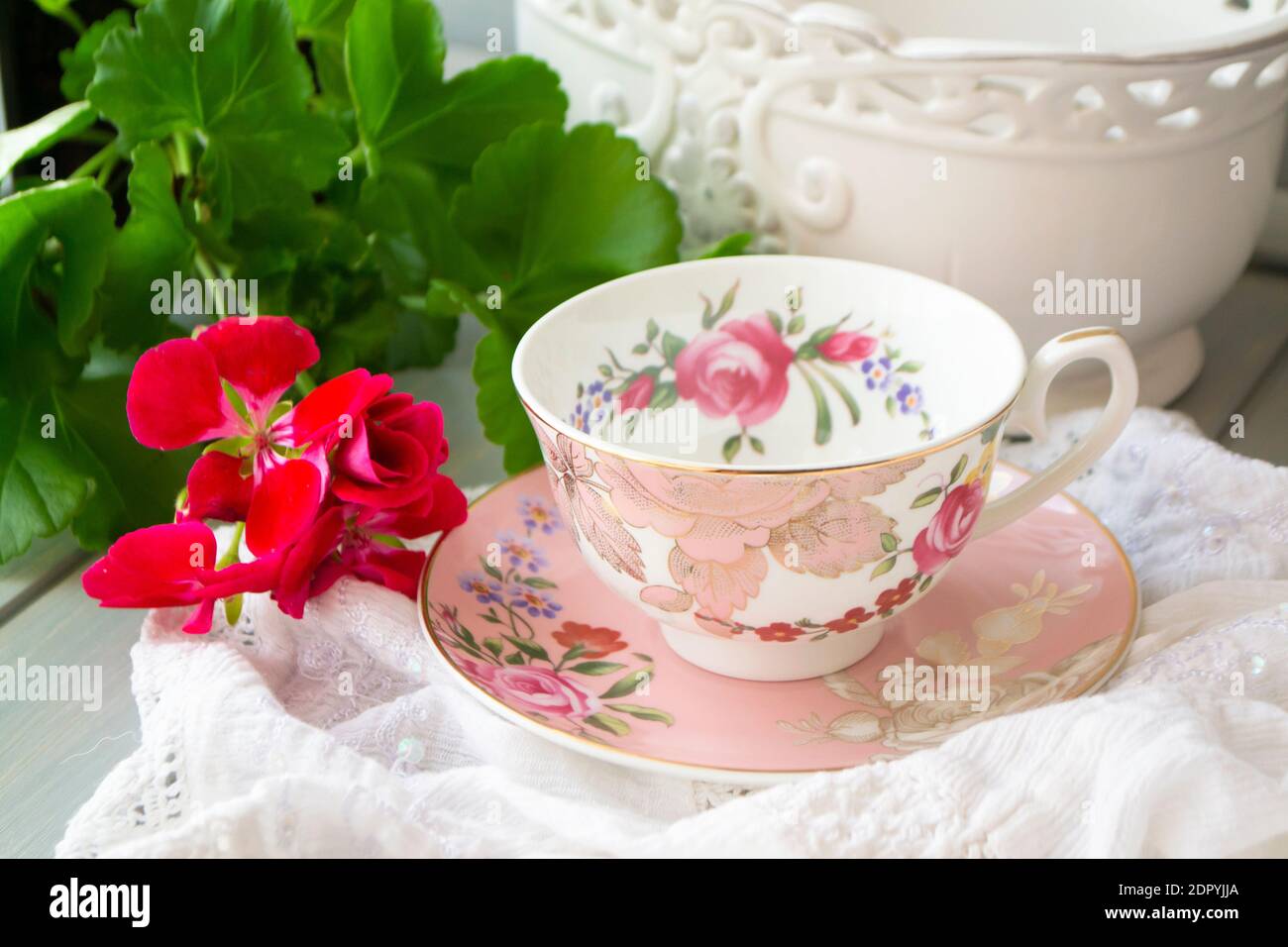 Pink vintage retro cup close up with Geranium flower on white vintsge napkin Stock Photo
