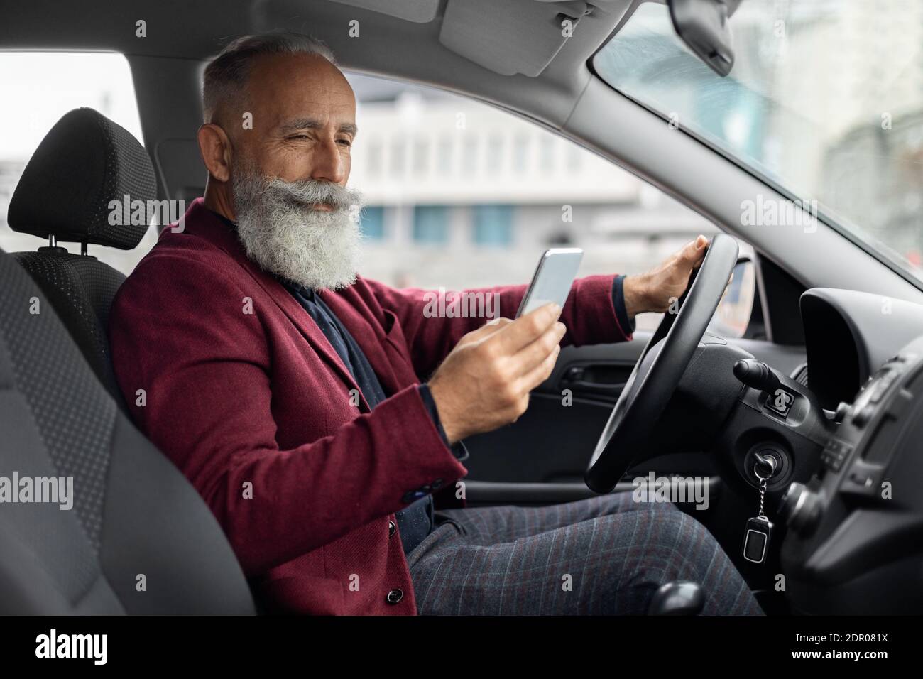 Elderly man driving new car, using mobile phone Stock Photo