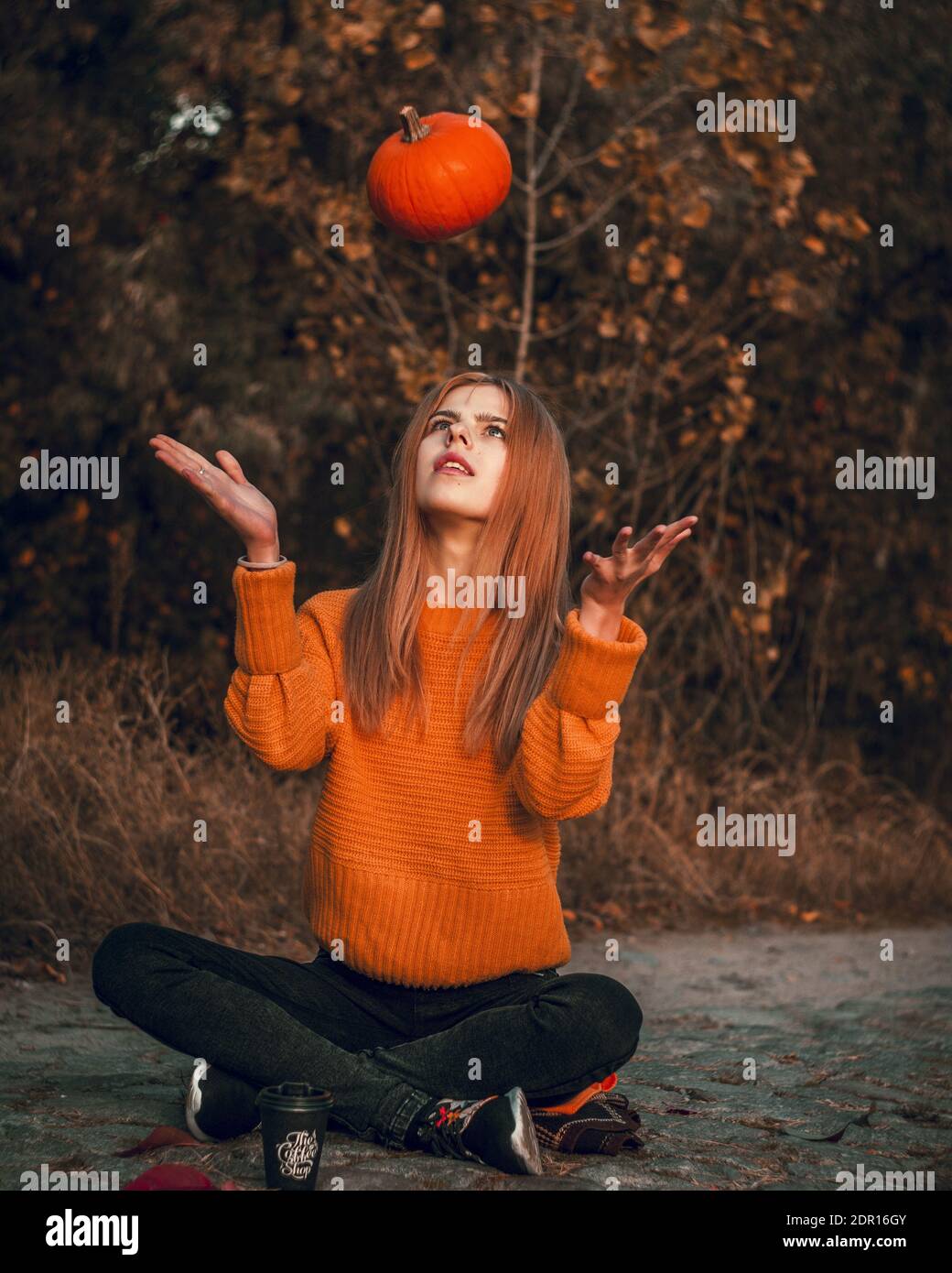 Full Length Of Young Woman Holding Pumpkin Sitting Against Trees Stock Photo