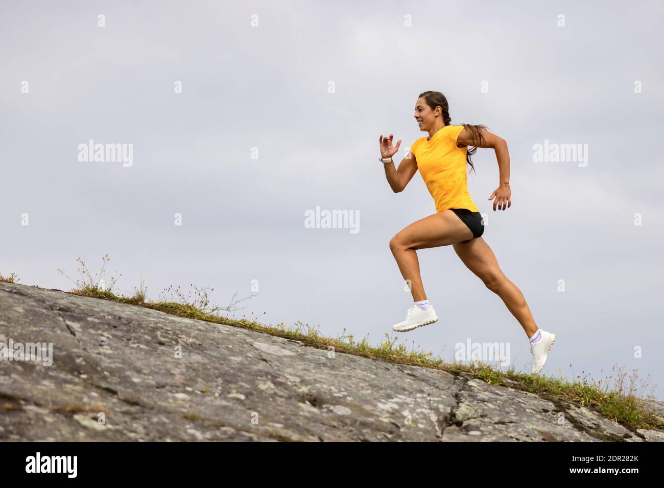 Side view of fitness woman doing high-intensity running on mountainside by the sea Stock Photo