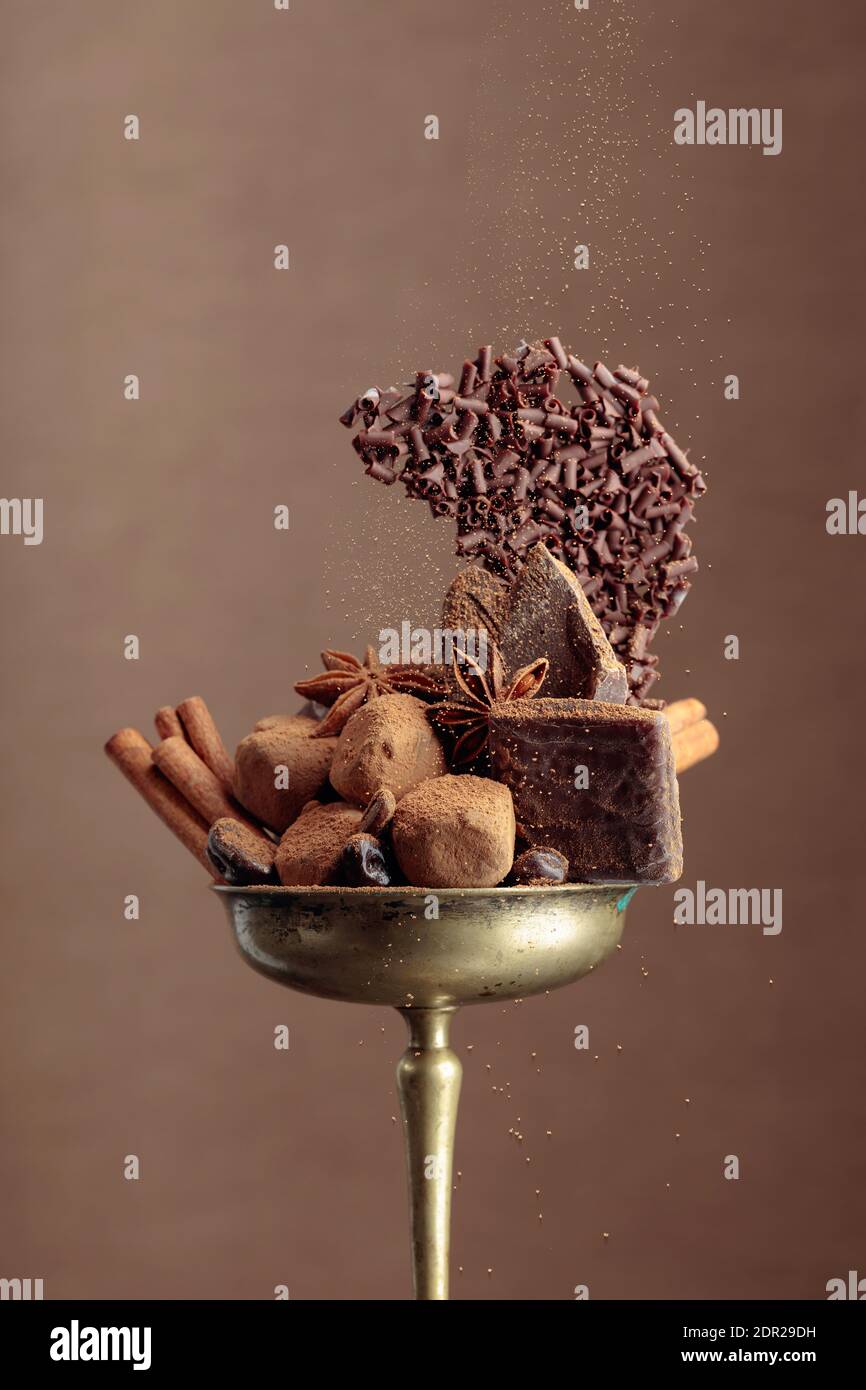 Various chocolates with ingredients.  In an old brass bowl candy, coffee beans, cinnamon, anise, and pieces of broken black chocolate. Copy space. Stock Photo