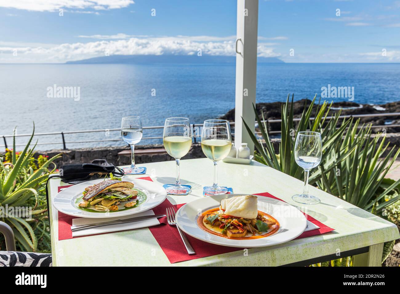 Plates of fish, sea bass and hake with glasses of white wine on a table in the Restaurant Pergola on the seafront in Puerto Santiago, Tenerife, Canary Stock Photo