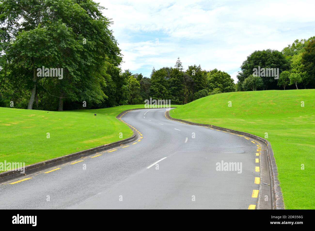 An asphalt road surrounded by bright green hills and trees during ...
