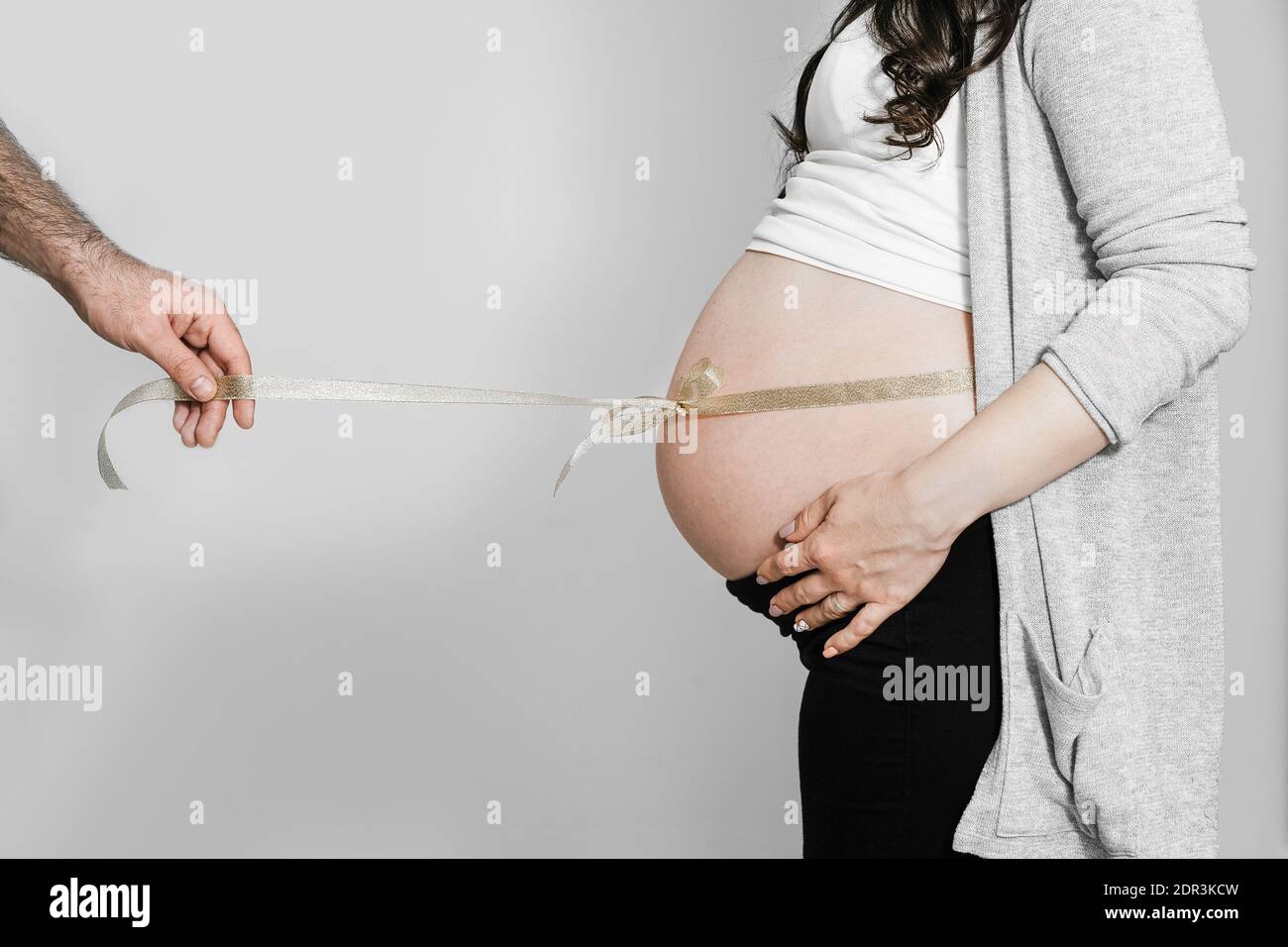 Cropped Hand Of Man Holding Ribbon Tied Up To Pregnant Woman Stomach  Against Wall Stock Photo - Alamy
