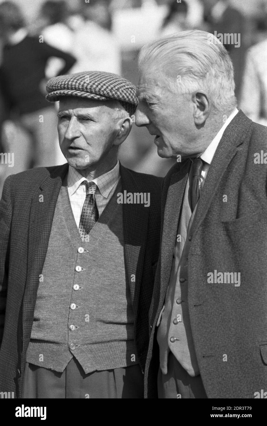 UK, England, Devonshire, Buckfastleigh, 1972. Point-to-Point races were held at  Dean Court on the Dean Marshes, close to the A38 between Plymouth and Exeter. Two traditional country gentlemen (probably farmers) talking. They are wearing a jacket, waistcoat, tie and one has a wool tweed flat cap on his head. Stock Photo