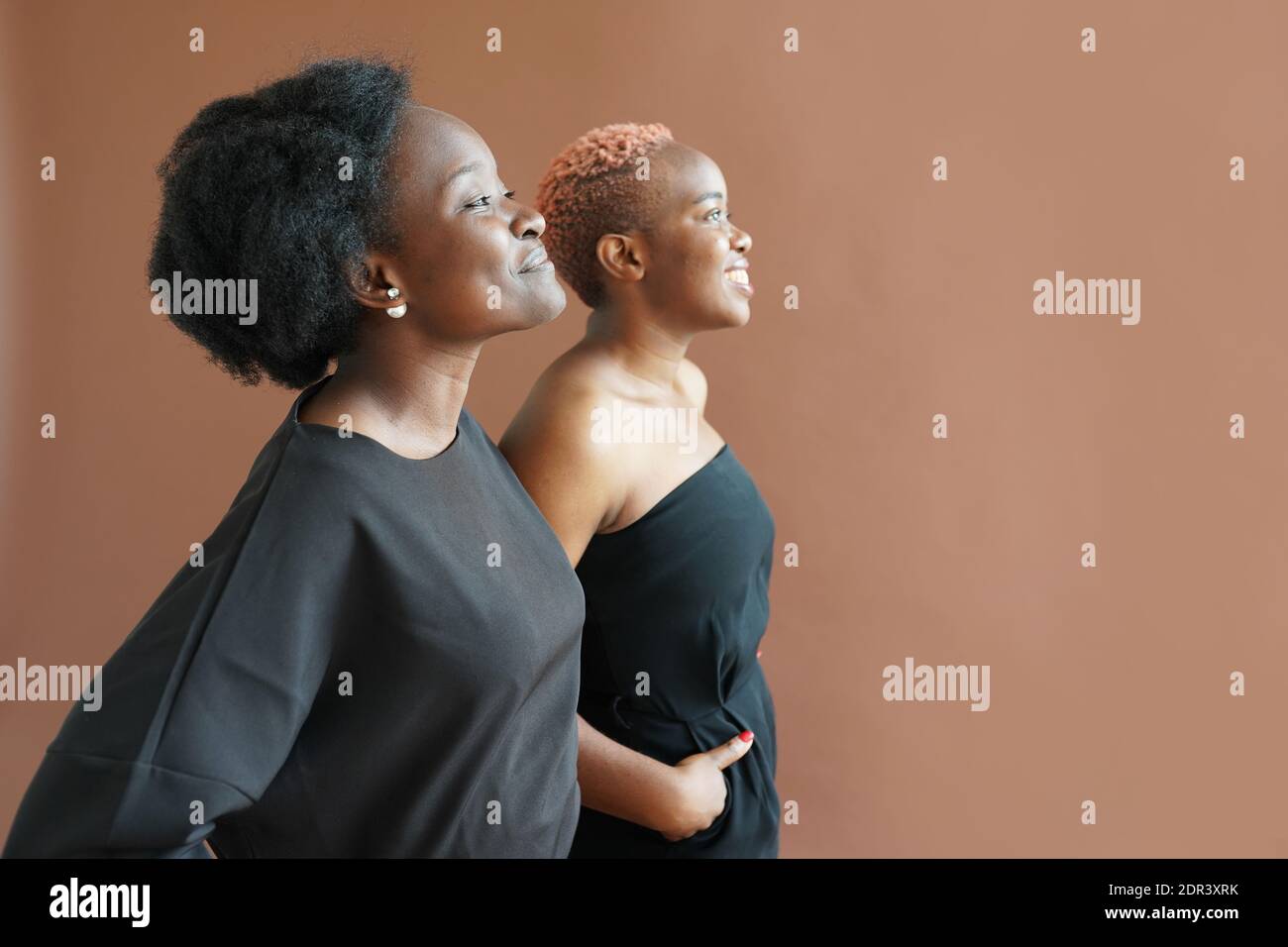 Two african friends are looking in the same direction on brown studio background, BLM Stock Photo