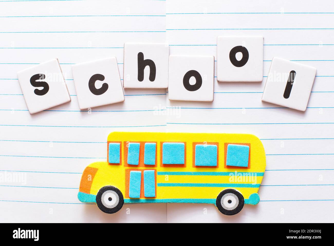 Word School written by black printed letters on white sheets of paper and bright yellow toy school bus on notebook sheet background Stock Photo