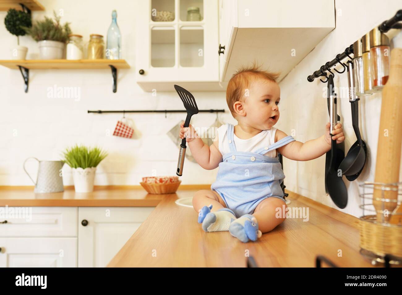 Baby playing with pans and spoons on kitchen table. One year old toddler infant hitting metal