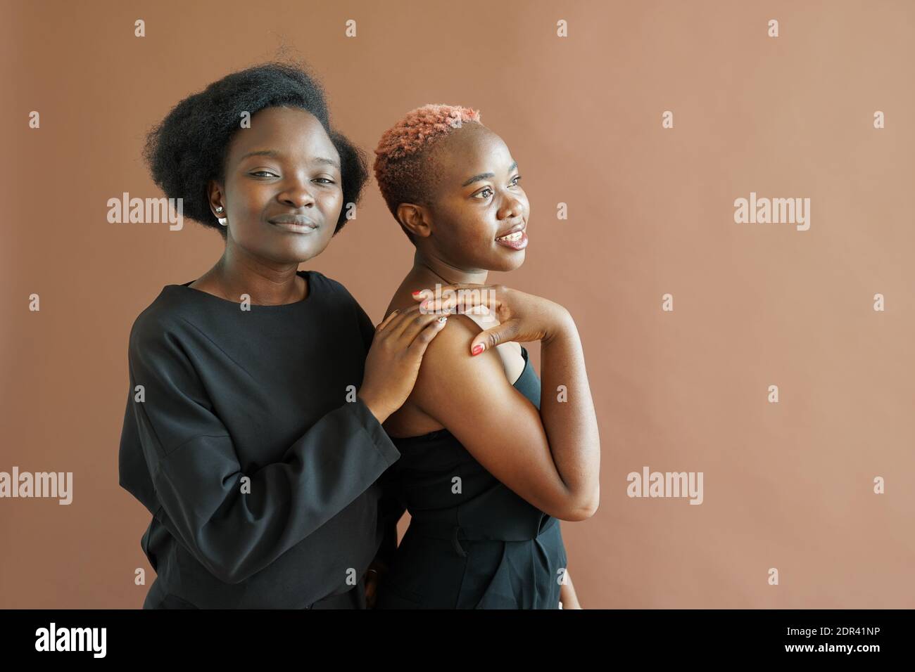 Two friendly african american girls gently hugging in the studio on brown background. BLM Stock Photo