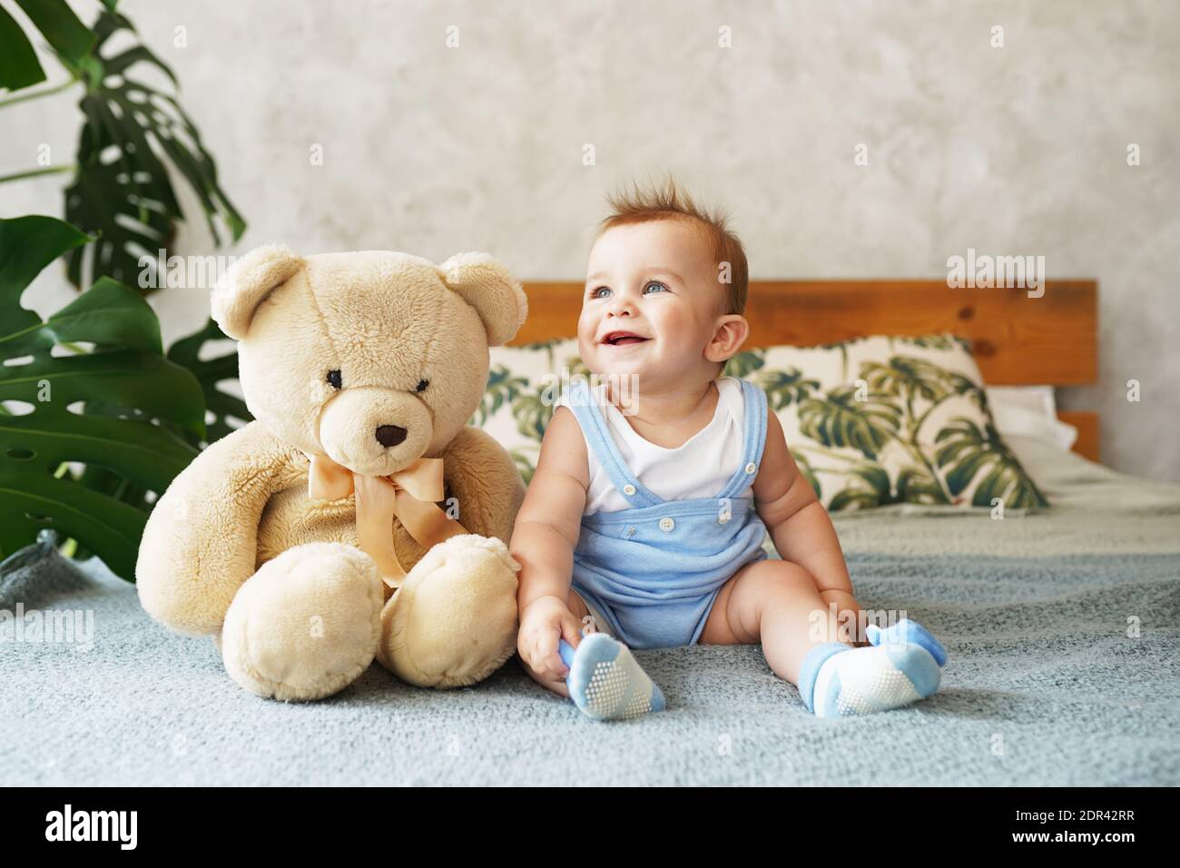Adorable little boy sitting on big bed with cute teddy bear and smiling ...