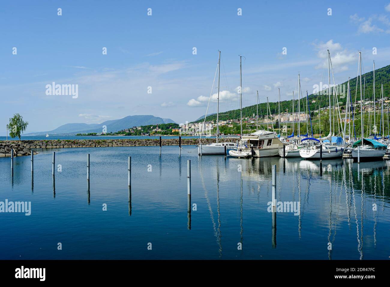 Small marina on the shores of Lake Neuchâtel. Very nice sunny weather. Rare clouds of fine weather in the blue sky. A few boats are moored. Stock Photo