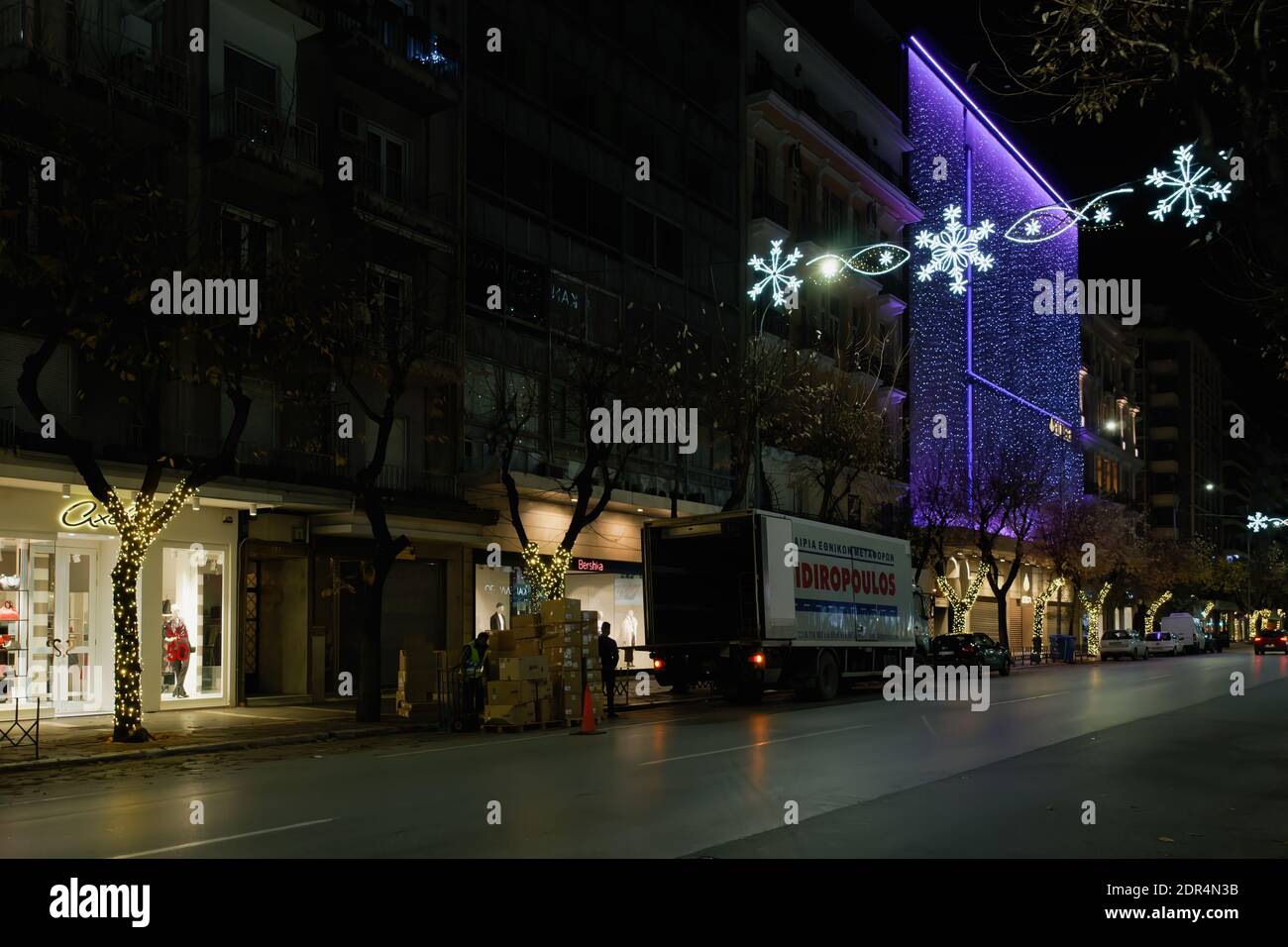 Thessaloniki, Greece - December 13 2020: Bershka brand shipment boxes unloading truck at night. Delivery men stacking packages of cardboards with clothes at Inditex Spanish retailer store entrance. Stock Photo