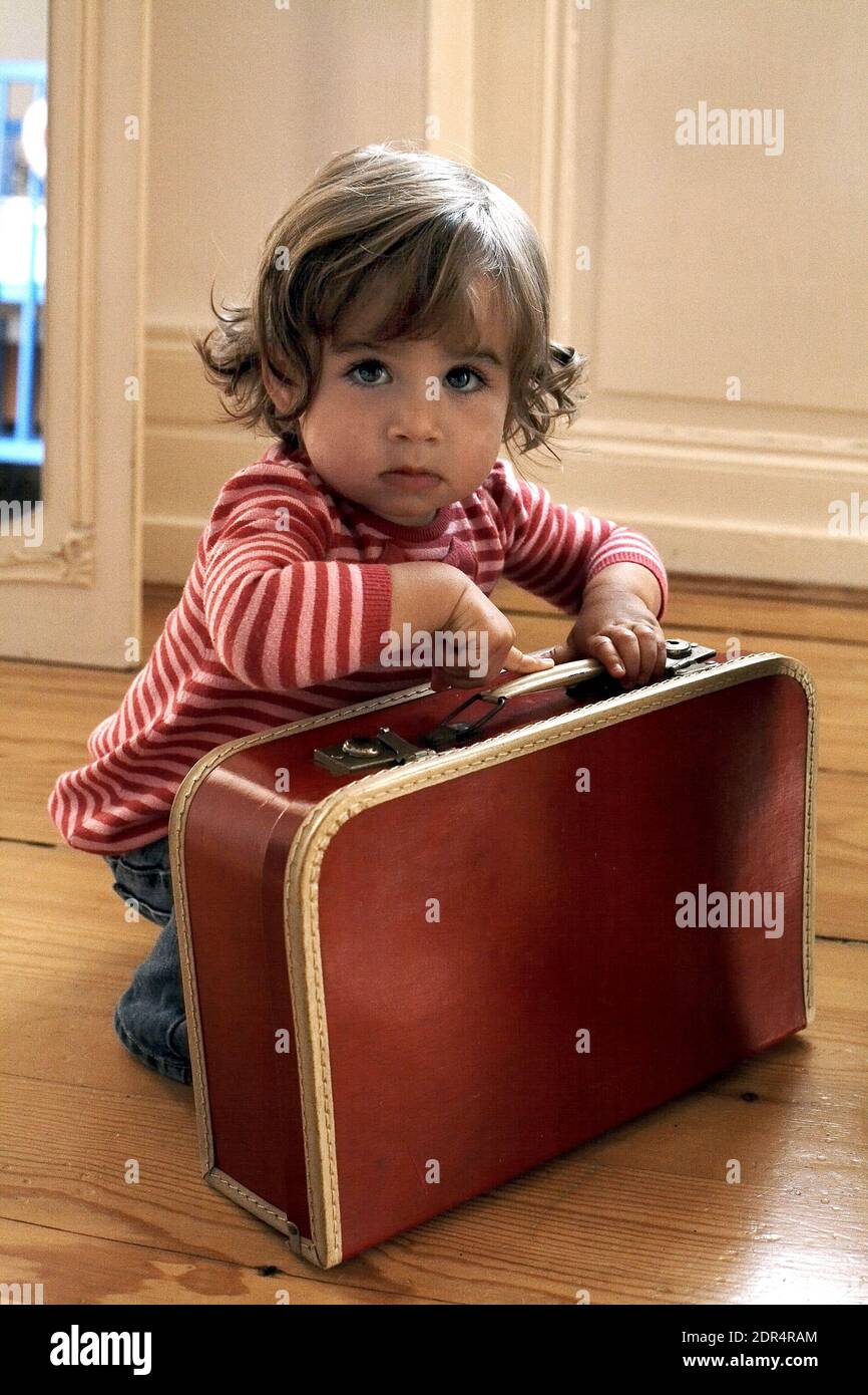 Germany/Frankfurt /Toddler girl (15-18 months) with a red  suitcase. Stock Photo