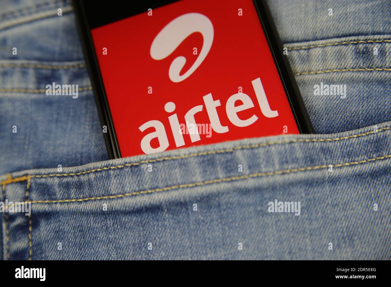 Viersen, Germany - May 9. 2020: Close up of smartphone screen in blue jeans pocket with logo lettering of indian mobile phone provider bharti Airtel ( Stock Photo