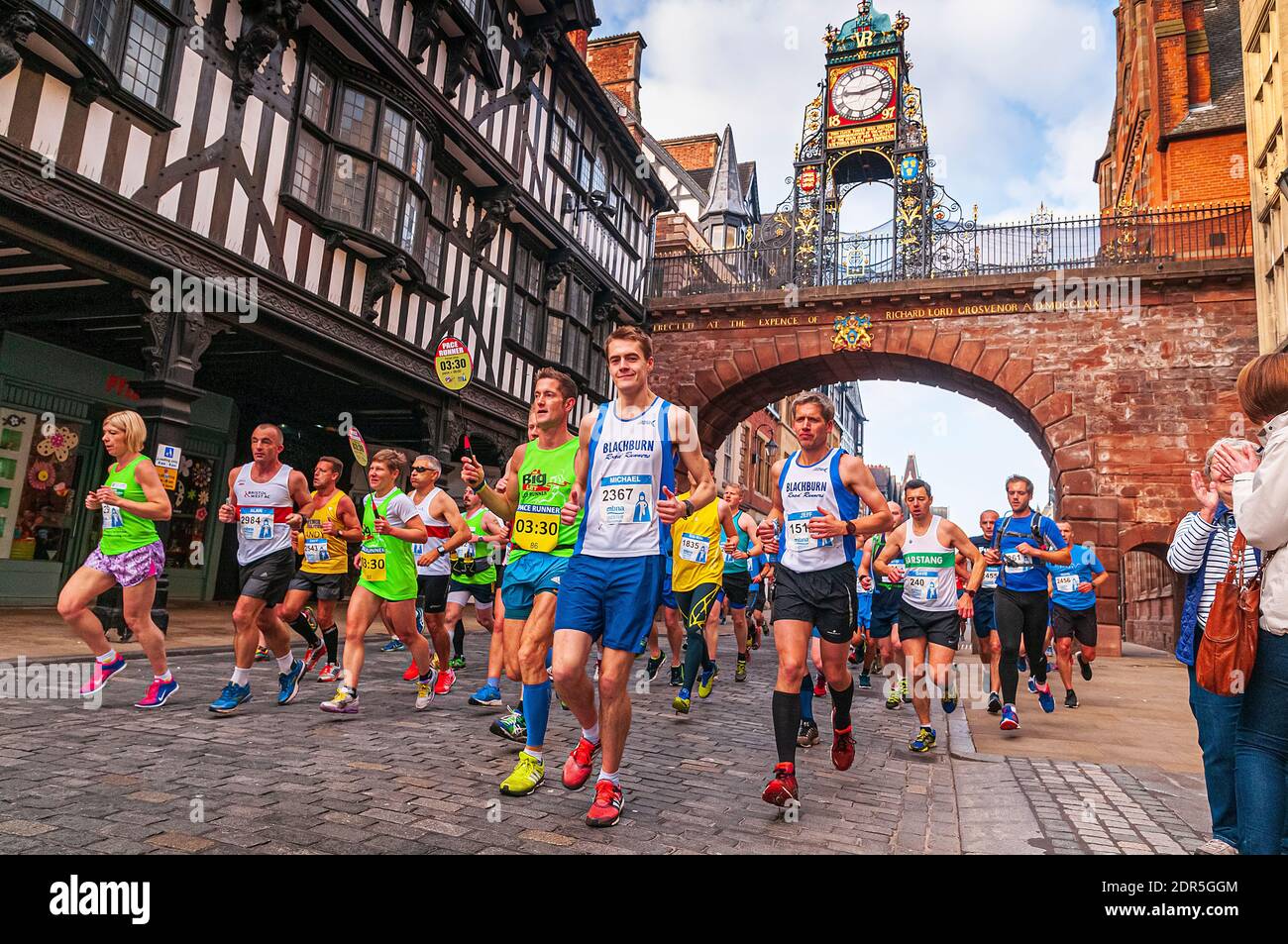 Marathon runners pass under the Eastgate clock tower in Chester Stock