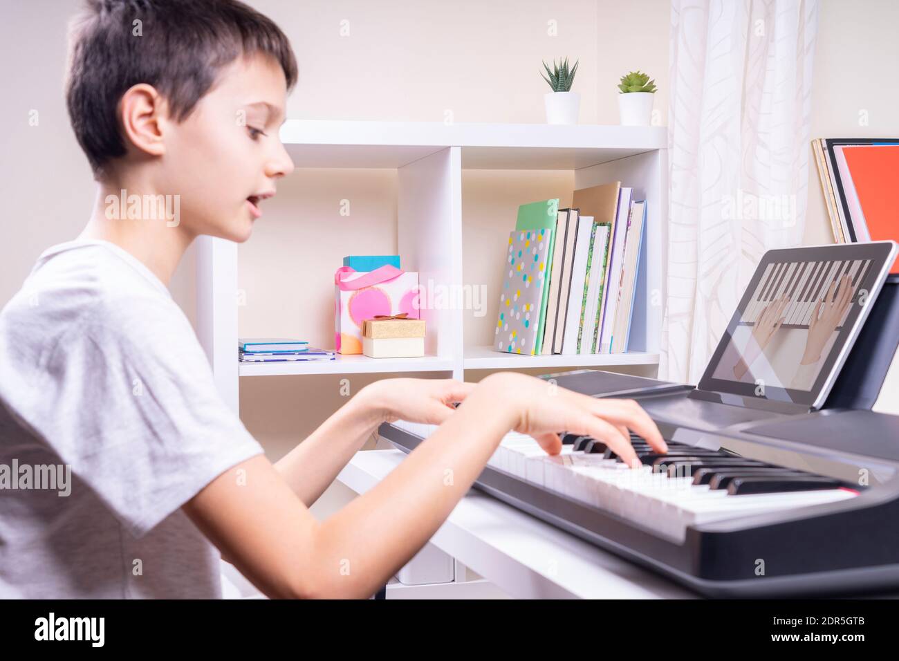 Online learning, remote education. Boy watching video at tablet computer,  playing digital piano and singing at home Stock Photo - Alamy
