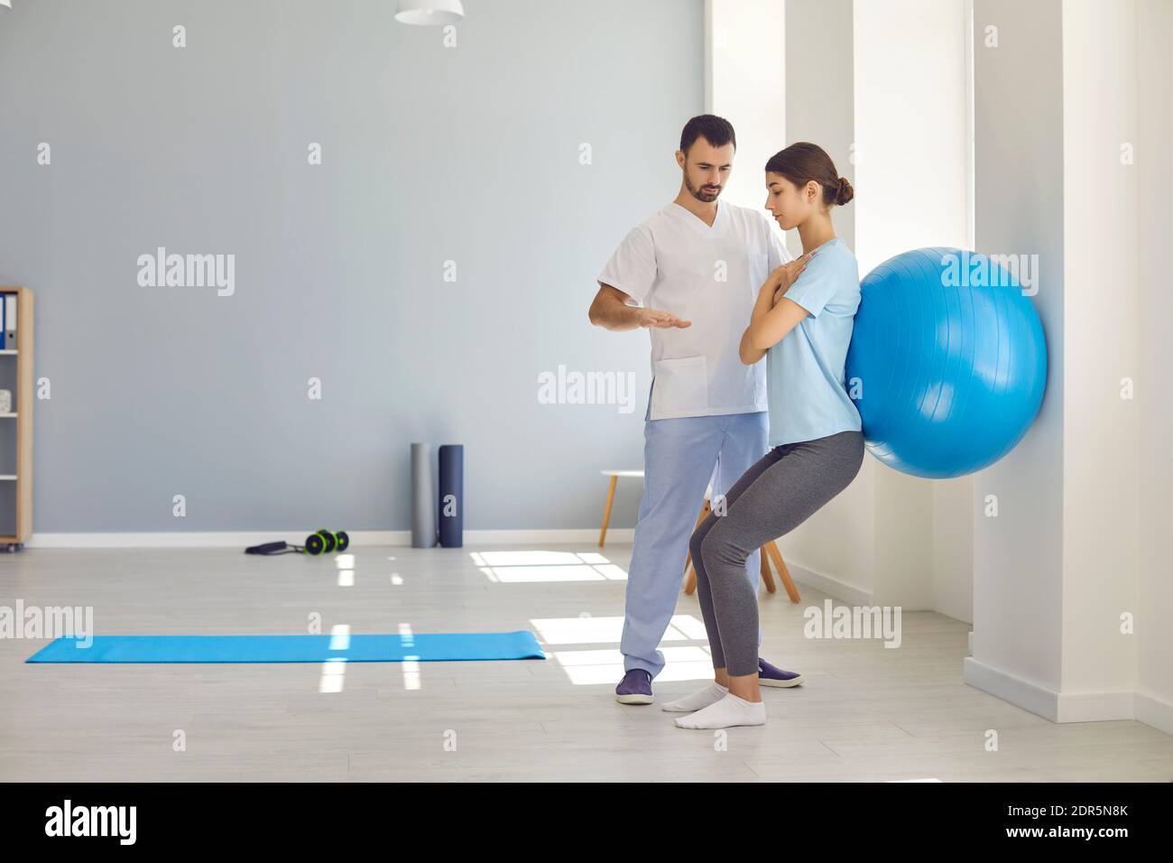 Professional osteopath controlling womans position during exercising with fitness ball Stock Photo