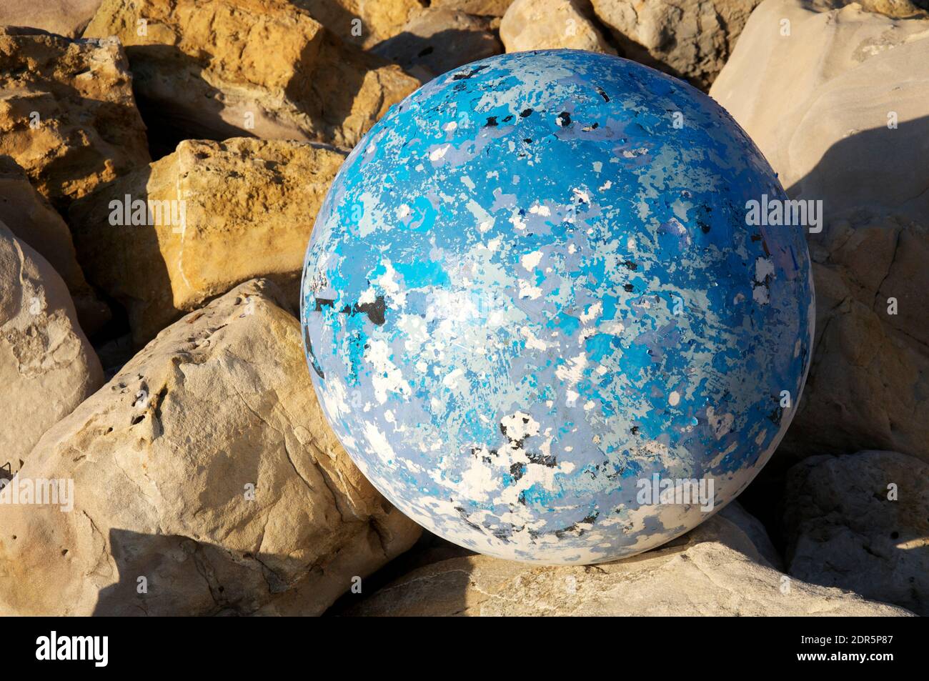 Surreal blue sphere against a rocky background. Flotsam and jetsam, a worn spherical Buoy textured with flaking paint, washed up on a beach in Dorset. Stock Photo