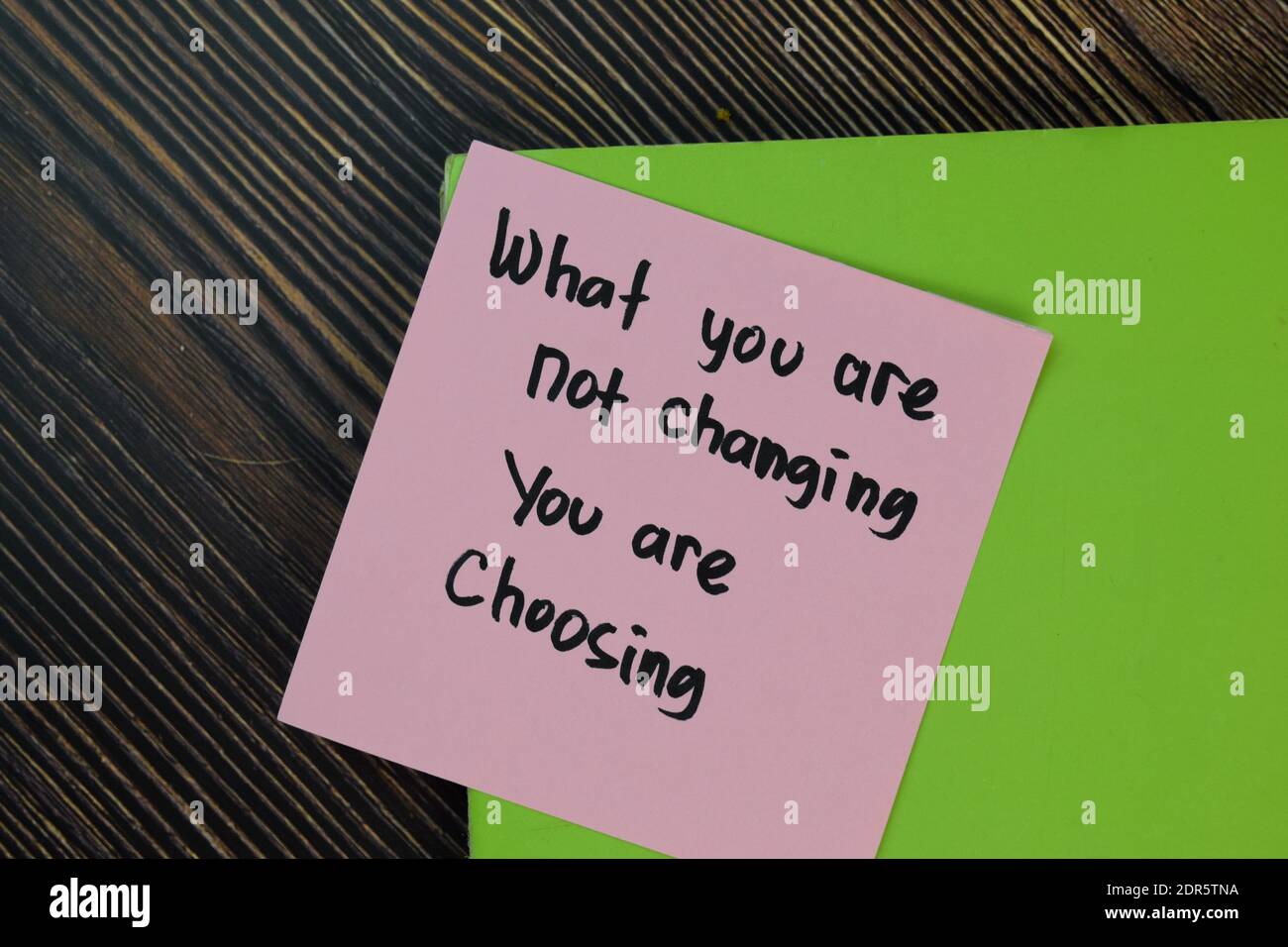 What you are not changing you are choosing write on sticky notes isolated on Wooden Table. Motivation concept Stock Photo