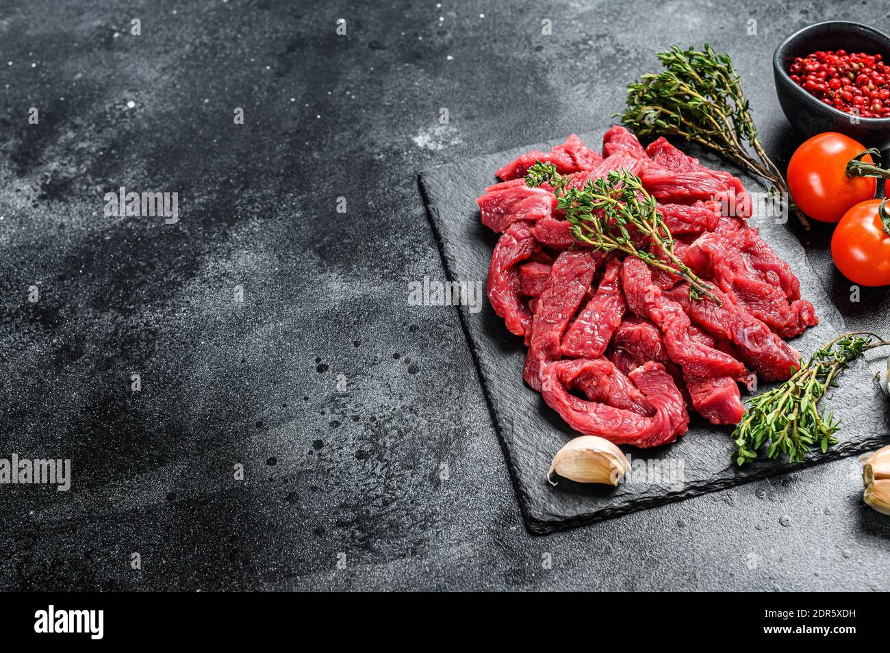 Raw meat cut into thin strips for beef Stroganoff. Black background