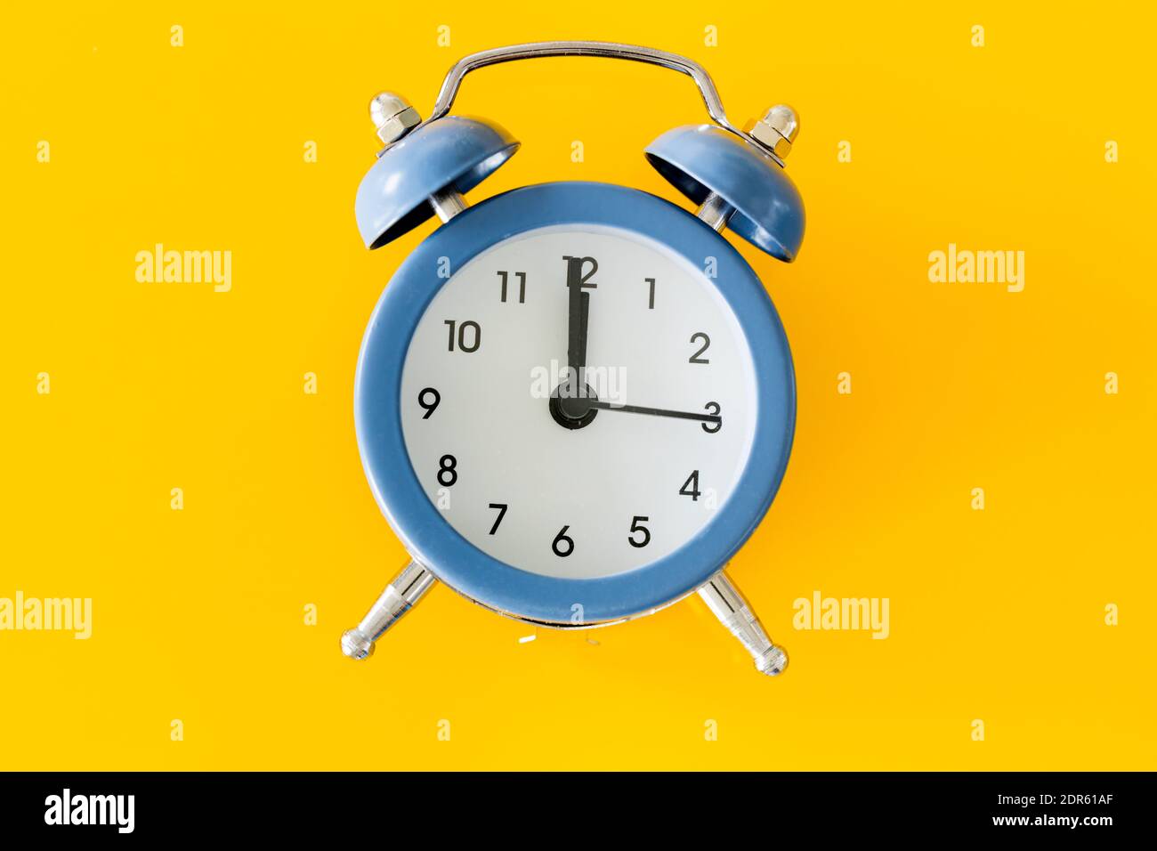 Stylish alarm clock showing five to twelve on a yellow background Stock Photo