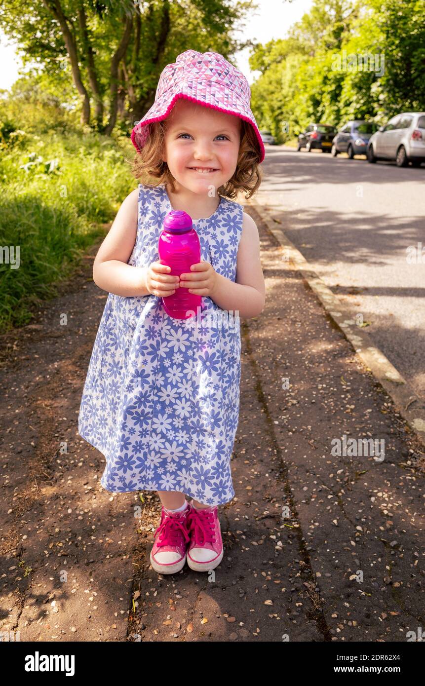 Happy smiling young two year old girl holding refillable water bottle outdoors in the street Stock Photo