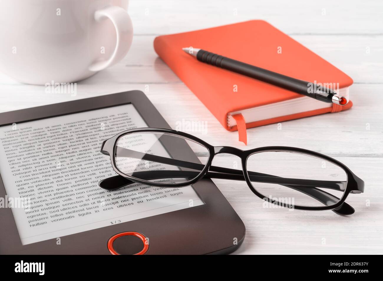 Eyeglasses on ereader and orange note pad on a white wooden desk