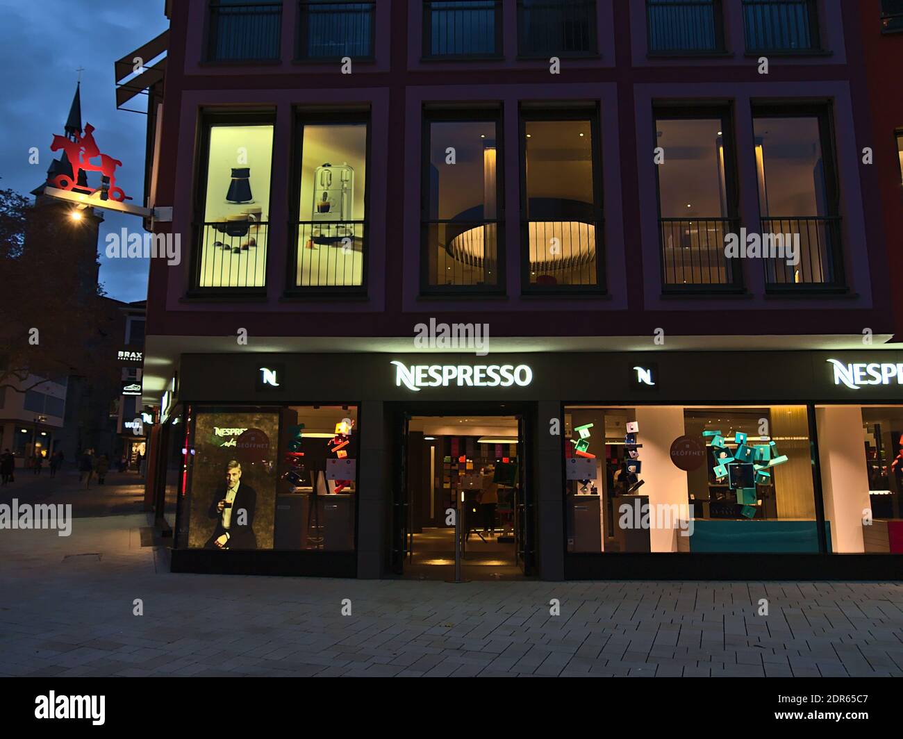 Front view of Nespresso (coffee capsules) retail store with illuminated shop windows on market place in downtown in the evening. Stock Photo