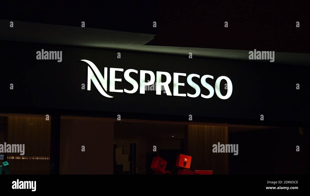 Illuminated white colored Nespresso (coffee capsules) logo above retail shop on market place in downtown in evening. Stock Photo