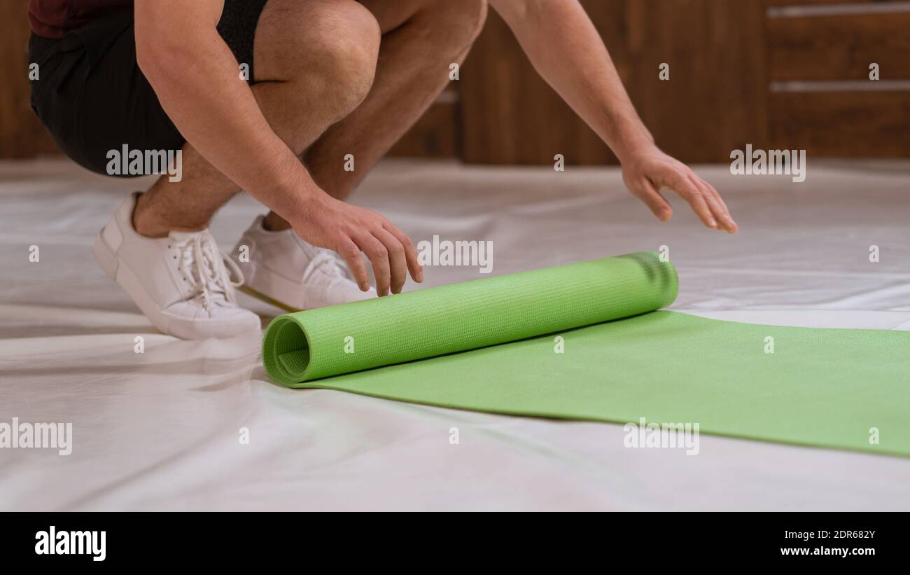 Fitness trainer young man, an athlete, unwinds a roll mat, preparing a place for sports. Determined guy doing physical training Stock Photo