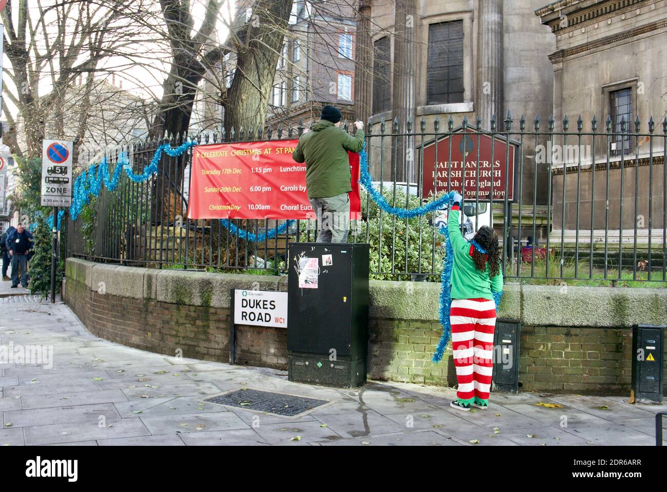 Woman dressed as Santa's elf and man decorate railing of St Pancras Church, London, in tinsel during Tier 4 restrictions with Christmas not cancelled Stock Photo