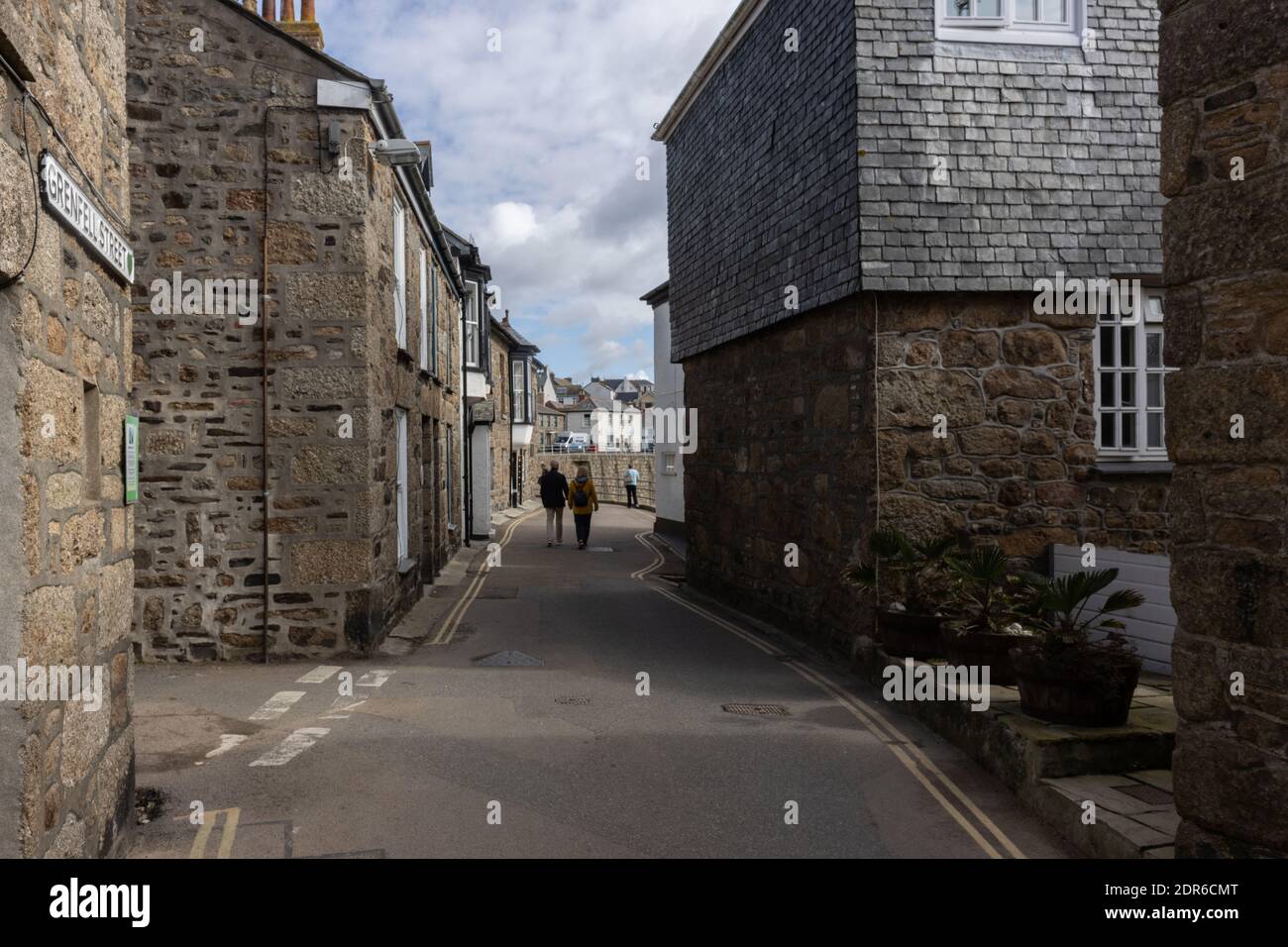 A couple walk hand in hand through a narrow street of granite cottages in traditional fishing village of Mousehole, Cornwall Stock Photo