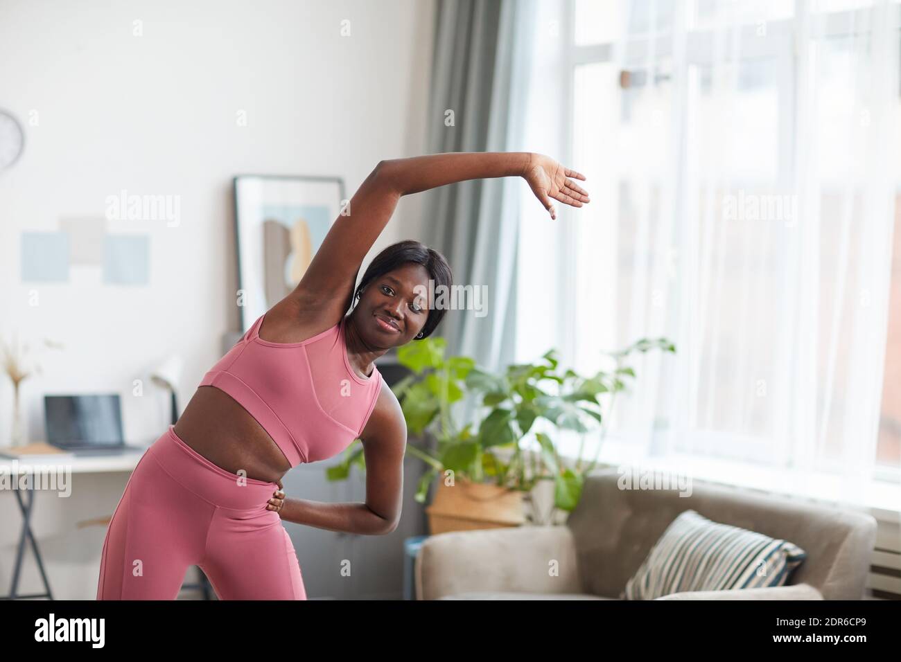 Portrait of smiling African-American woman wearing pink sportswear while stretching during workout at home, copy space Stock Photo