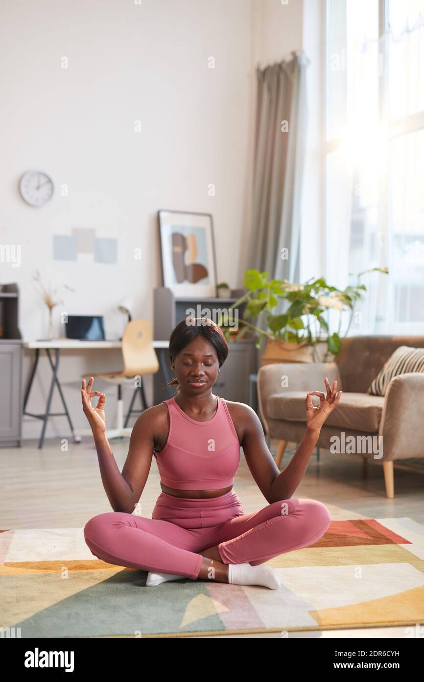 Vertical portrait of young African-American woman wearing pink sportswear during yoga workout at home Stock Photo
