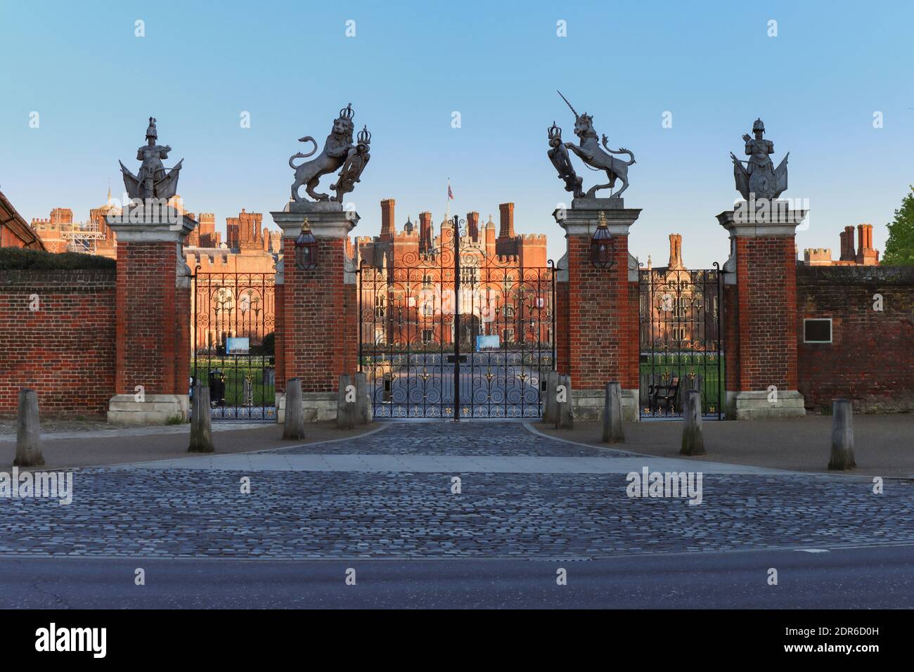 Red brick Tudor Facade of Hampton Court Palace seen through its imposing wrought iron entrance gates as the sun sets Stock Photo
