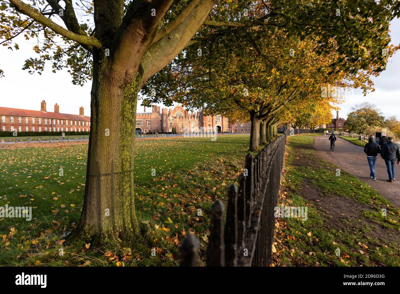 Bright red Tudor Facade of Hampton Court Palace seen through trees that are alongside the river Thames footpath side Stock Photo