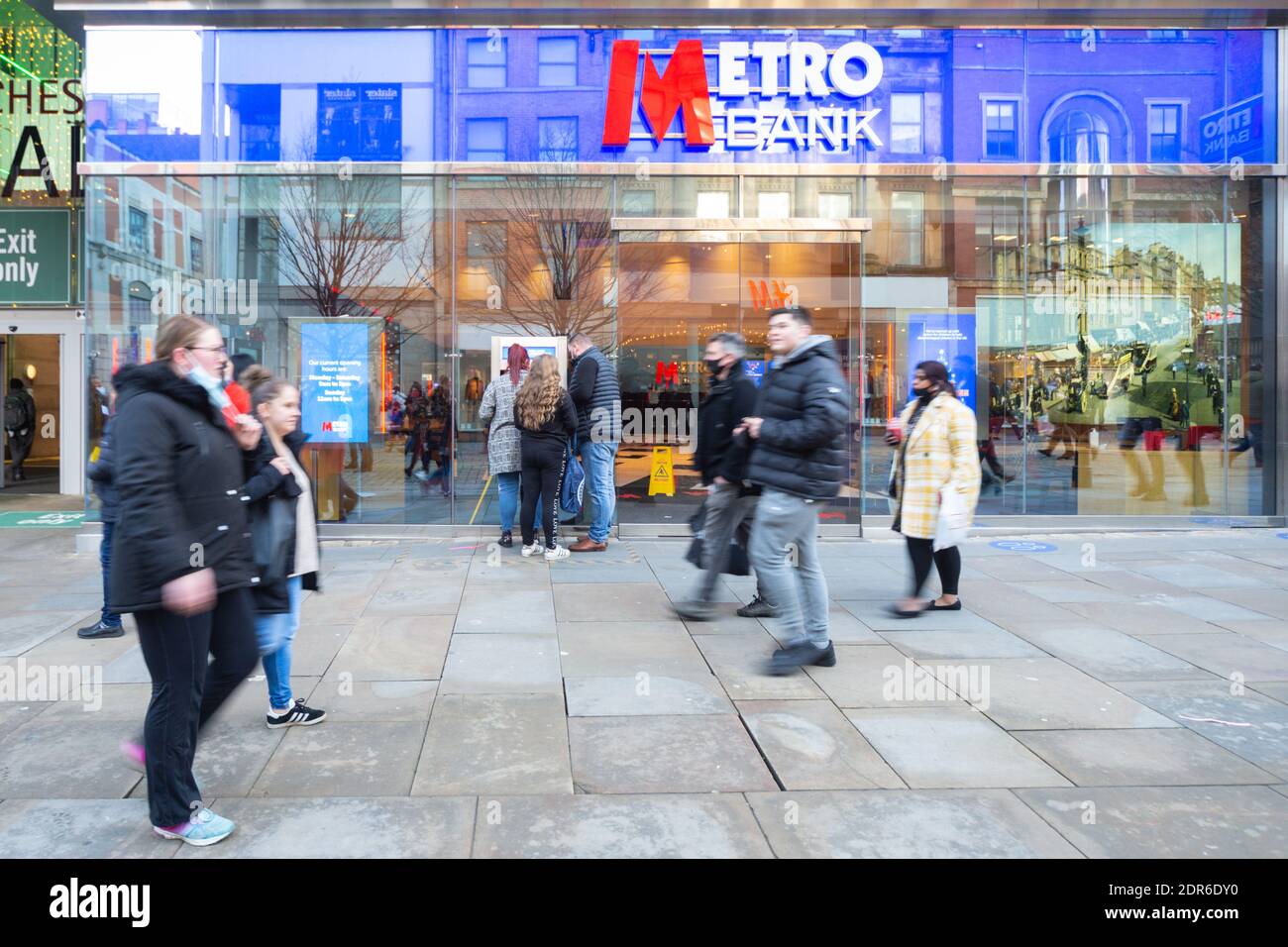 Metro Bank storefront, facade, Market Street, Manchester City Centre. Three people use an atm or cash machine while pedestrians walk by. December 2020 Stock Photo