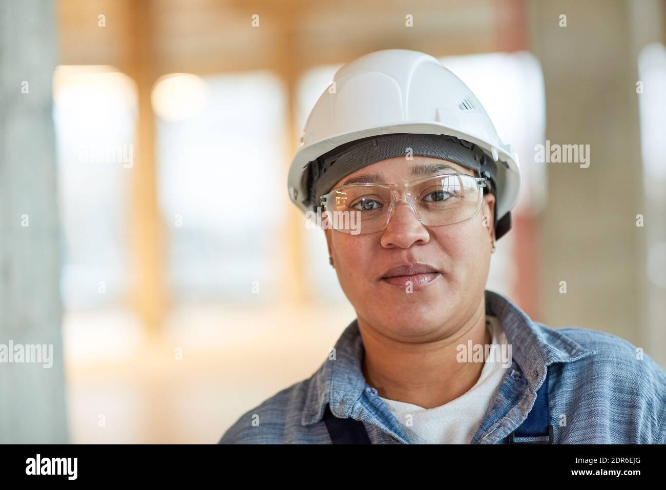 Front view portrait of female worker wearing hardhat and looking at camera while standing on construction site, copy space Stock Photo