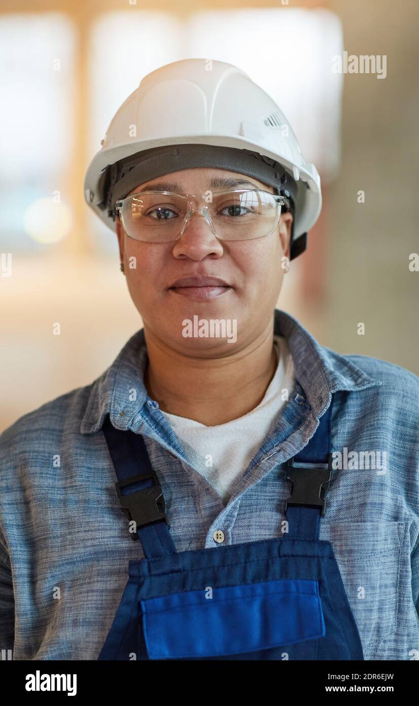 Vertical portrait of female worker wearing hardhat and looking at camera while standing on construction site Stock Photo