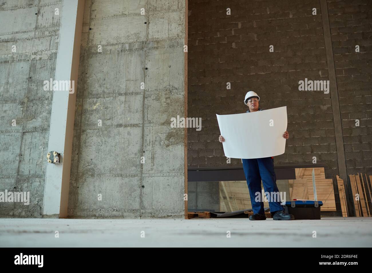 Wide angle view of female construction worker holding plans while working in apartment building, copy space Stock Photo