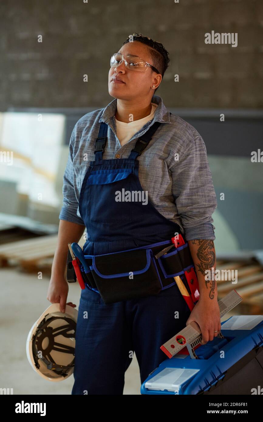Vertical portrait of modern female worker holding toolbox while standing on construction site Stock Photo