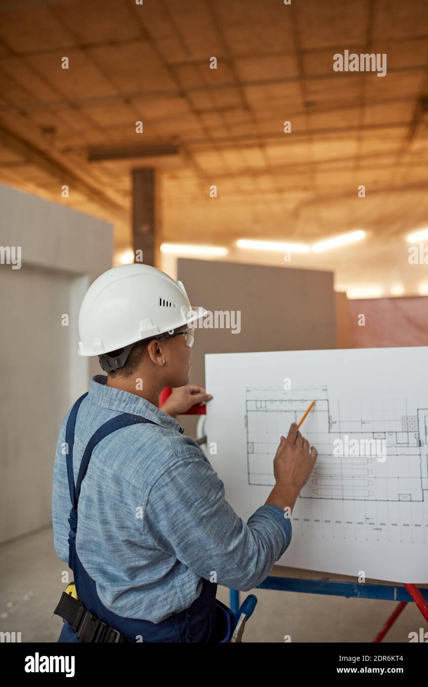 Vertical back view portrait of female engineer inspecting plans while