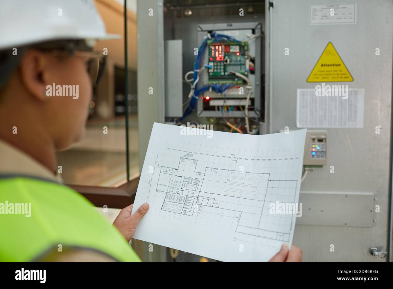 Female worker holding blueprints while inspecting electrical switchboard at construction site, copy space Stock Photo