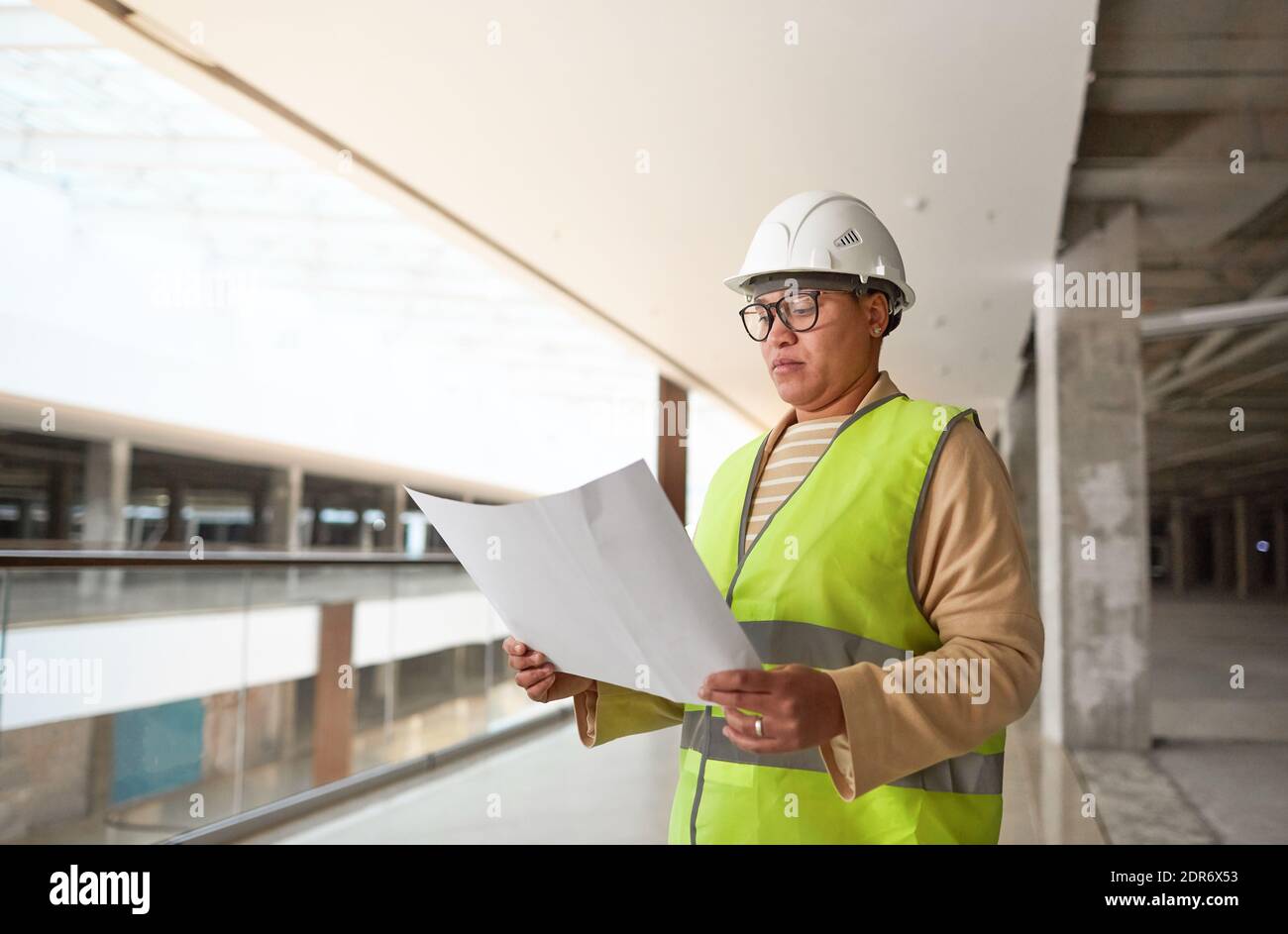 Waist up portrait of mixed-race female engineer holding blueprints while working on construction site, copy space Stock Photo