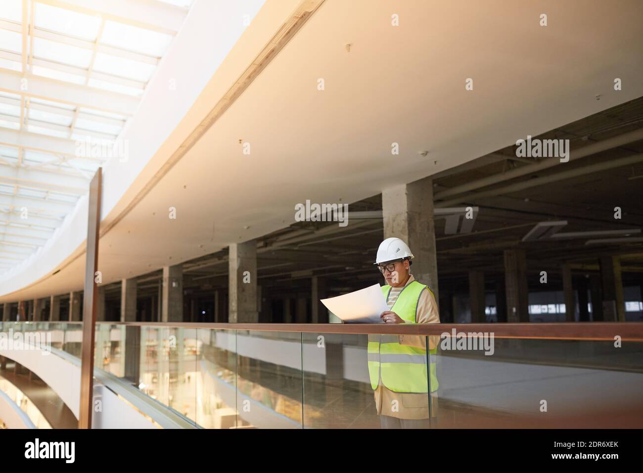 Wide angle portrait of mixed-race female engineer holding blueprints while working on construction site, copy space Stock Photo