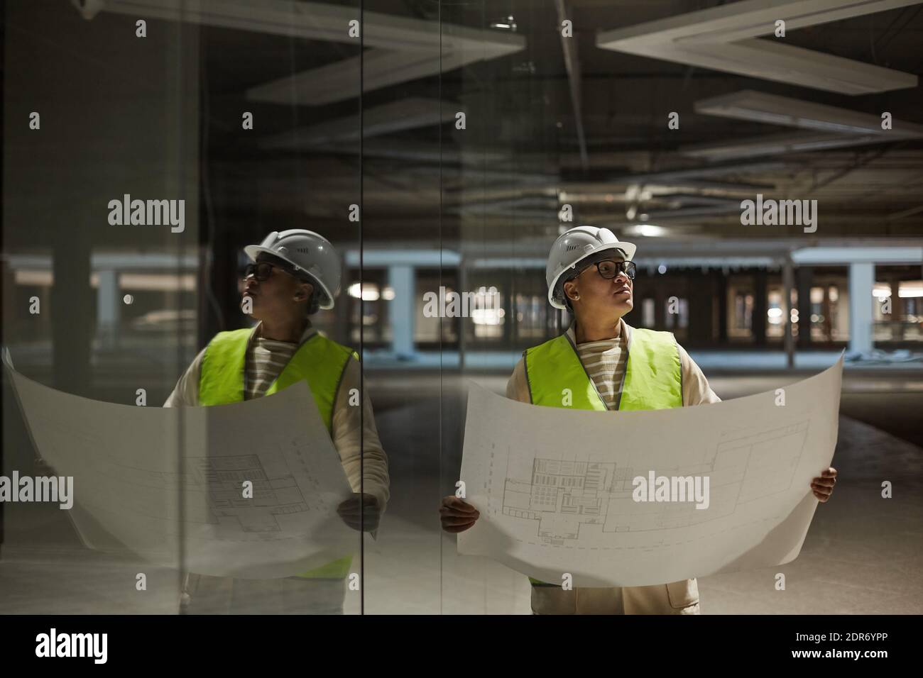 Waist up portrait of female engineer holding blueprints while inspecting base of building at construction site, copy space Stock Photo