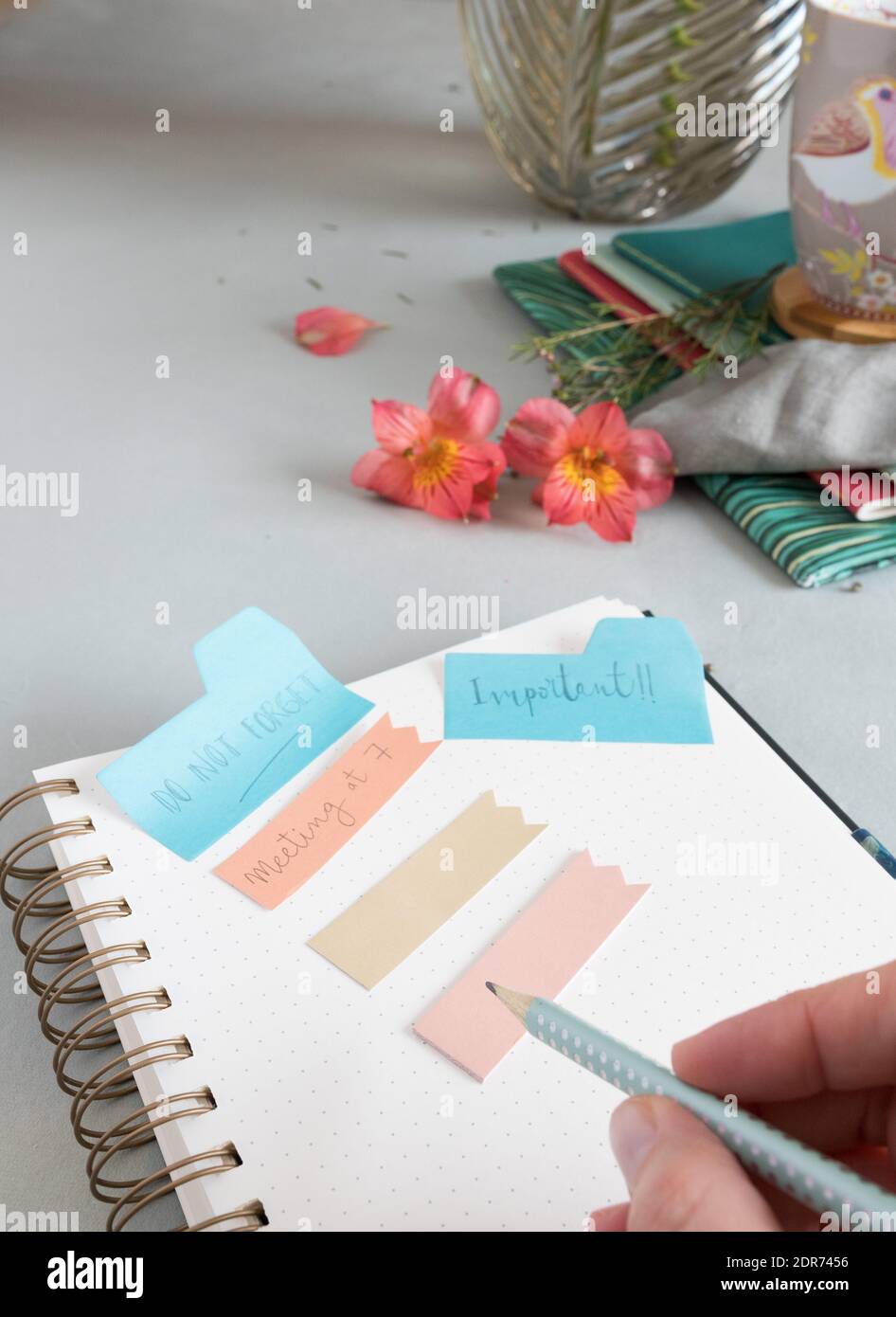 Empty spiral notebook with a dotted pencil held by a woman hand and several reminder notes at the top of it. Stock Photo